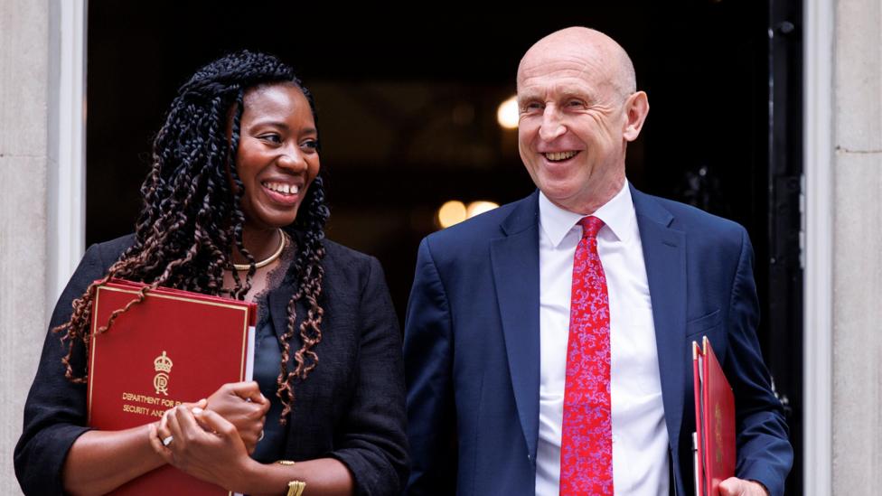 Miatta Fahnbulleh and John Healey grinning as they walk out of the door at 10 Downing Street clutching red ministerial folders