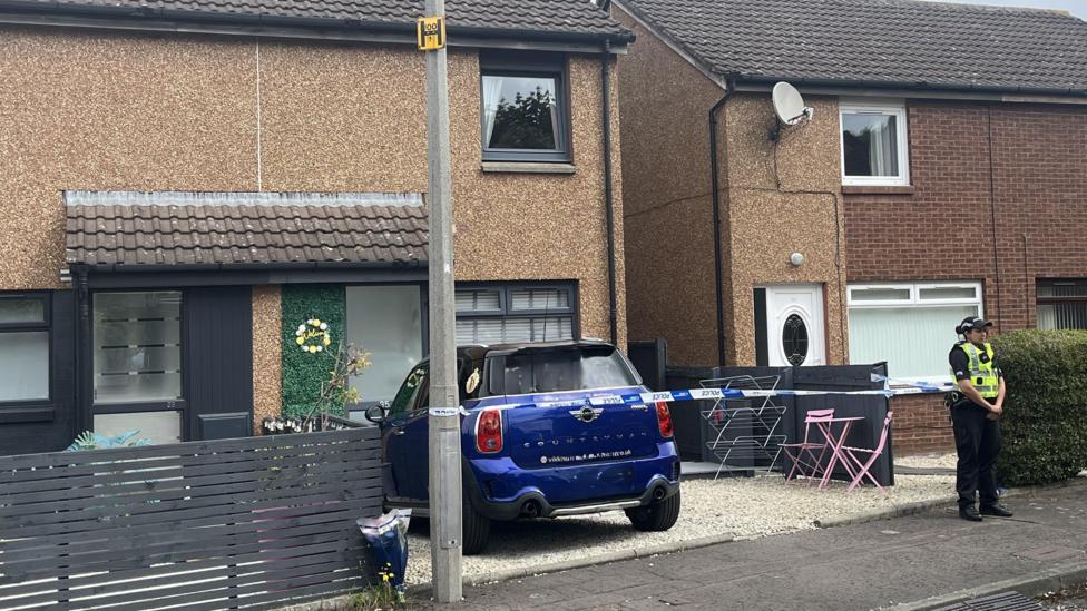 A female police officer stands outside a cordoned-off house.