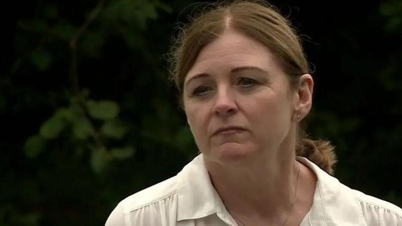 Debbie Adlam wearing a white blouse, in front of a dark background of shrubs