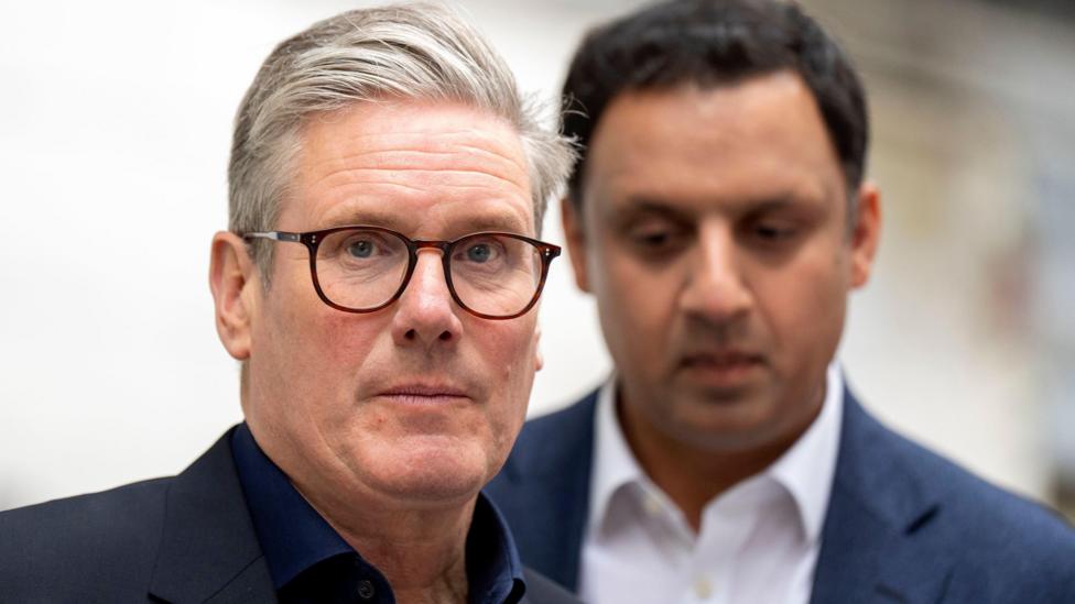 Sir Keir Starmer, with grey hair and glasses standing in front of Anas Sarwar with black hair.