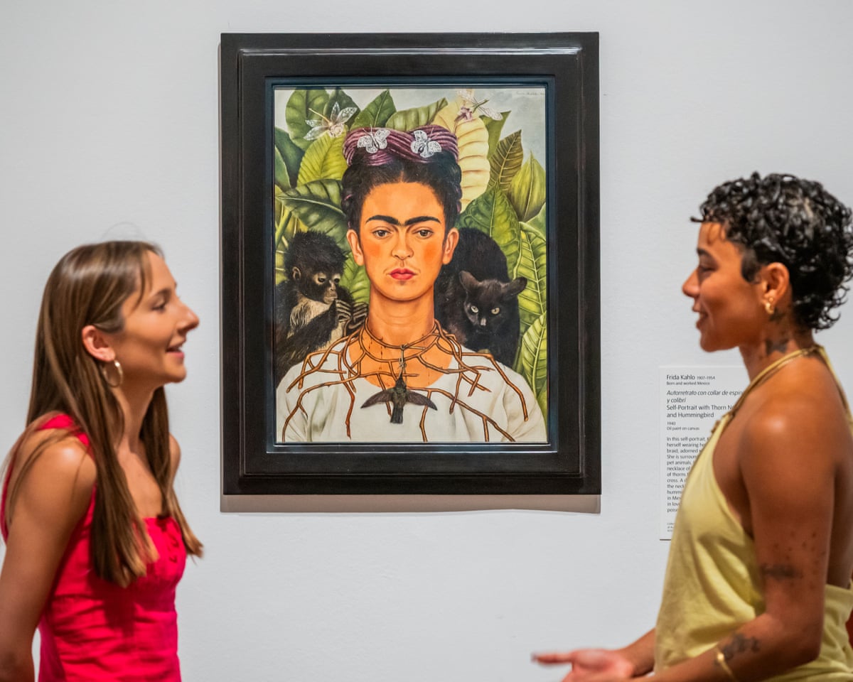 Two women in discussion before a portrait of Mexican artist Frida Kahlo.