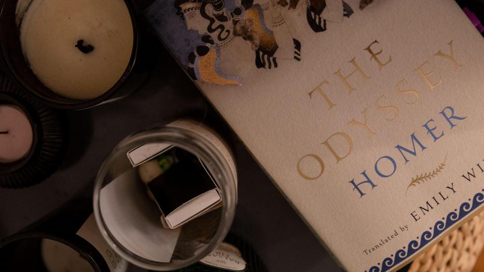 A photo of a copy of Emily Wilson's translation of The Odyssey on a table along with a candle and other items