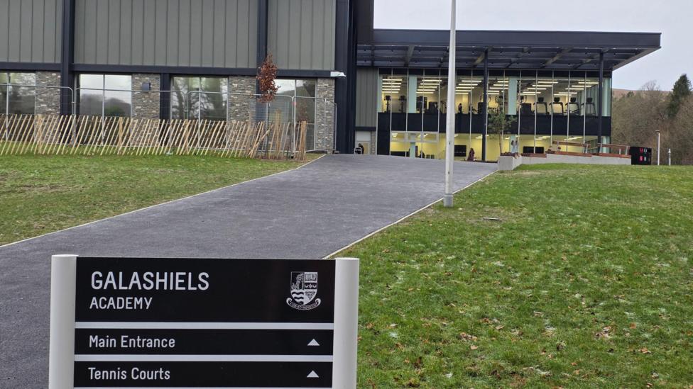A sign for Galashiels Academy in the foreground with a path leading up to a modern school building with a flat roof