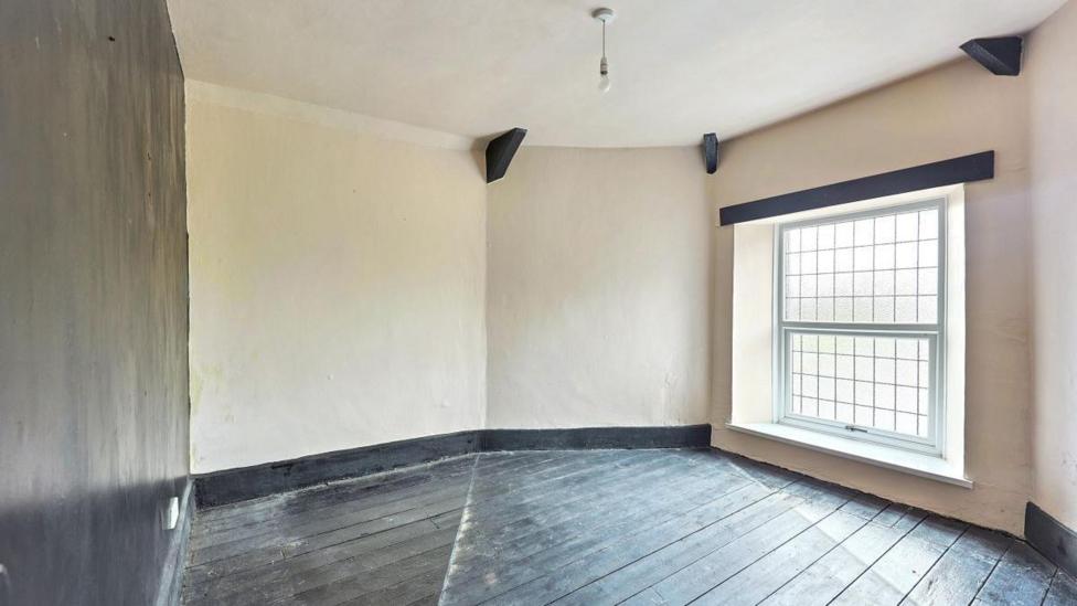 An empty bedroom with dark wooden floors and a large window. 