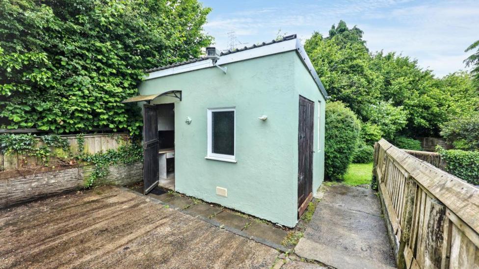A green outbuilding with black doors outside in the garden. 