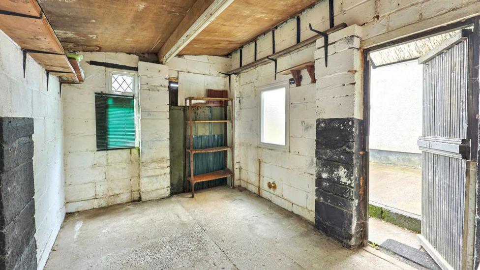 Inside the outbuilding. It has white brick walls with a few brown shelves. 