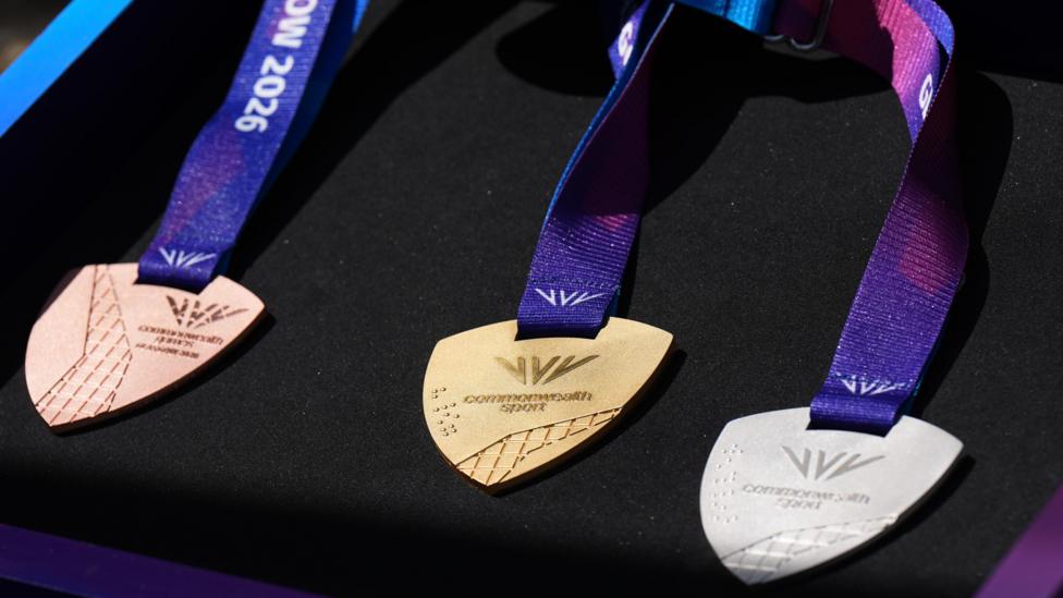 Bronze, gold and silver Commonwealth Games medals - with a purple ribbon -against a black backdrop.