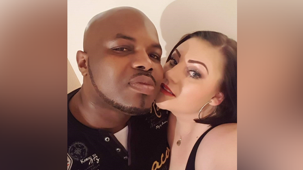 Eric and Rachel are seen smiling at the camera in a selfie. Eric has a shaved head with a short trimmed beard. Rachel has short dark hair and is wearing hoop earrings. 