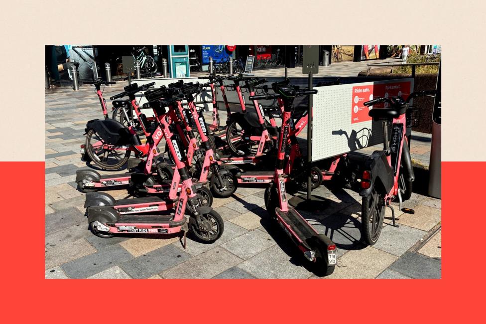 A designated e-scooter parking spot in Southampton. The orange e-scooters are parked on a pavement next to some railings. A sight reads: 