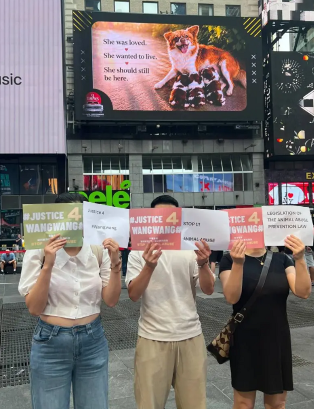 Three people standing before a billboard of Wang Wang, holding sheets of paper that read, 