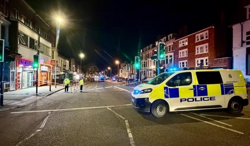A police van in front of police tape along a road with no traffic on.