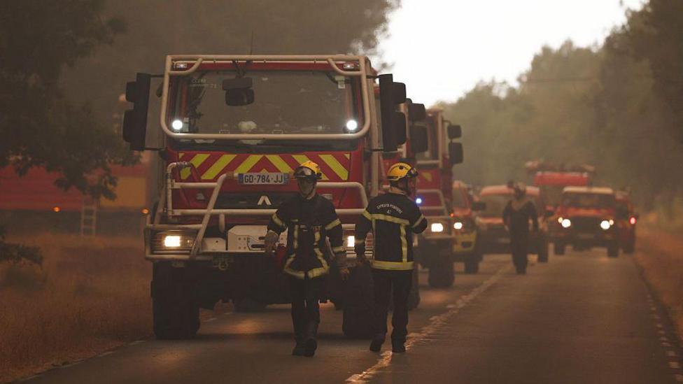 Lines of fire trucks on a road with hazy smoke in the air