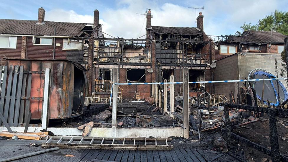 The back of a burnt out house with blue and white police tape across it