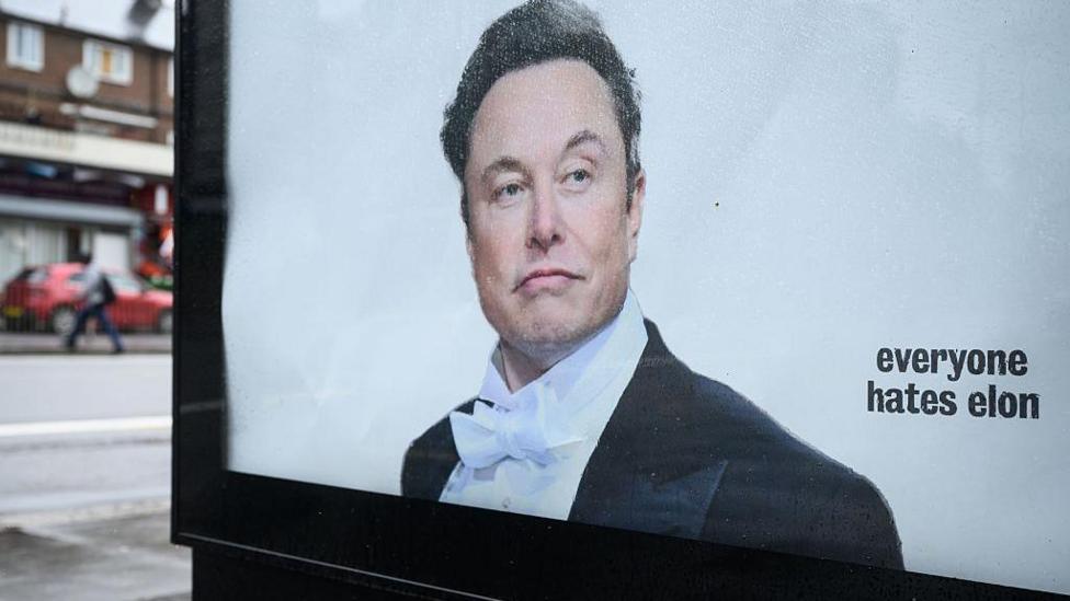 A poster of Musk wearing a suit and bow tie on an advertising display panel in London, with 