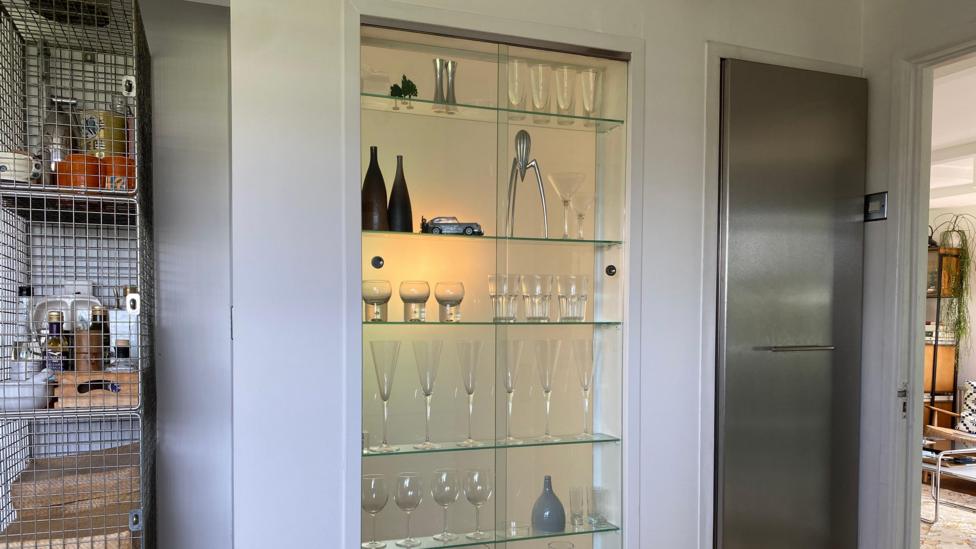 A glass cabinet that allows light into the room. It's filled with champagne and wine glasses and is backlit.