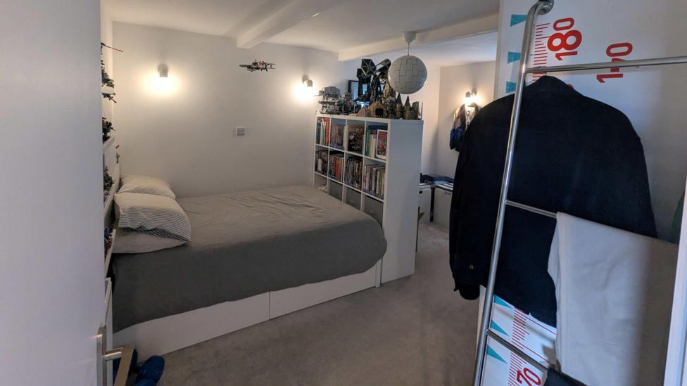 A clean teenage boy white room with a double bed and a shelf full of books and Lego.
