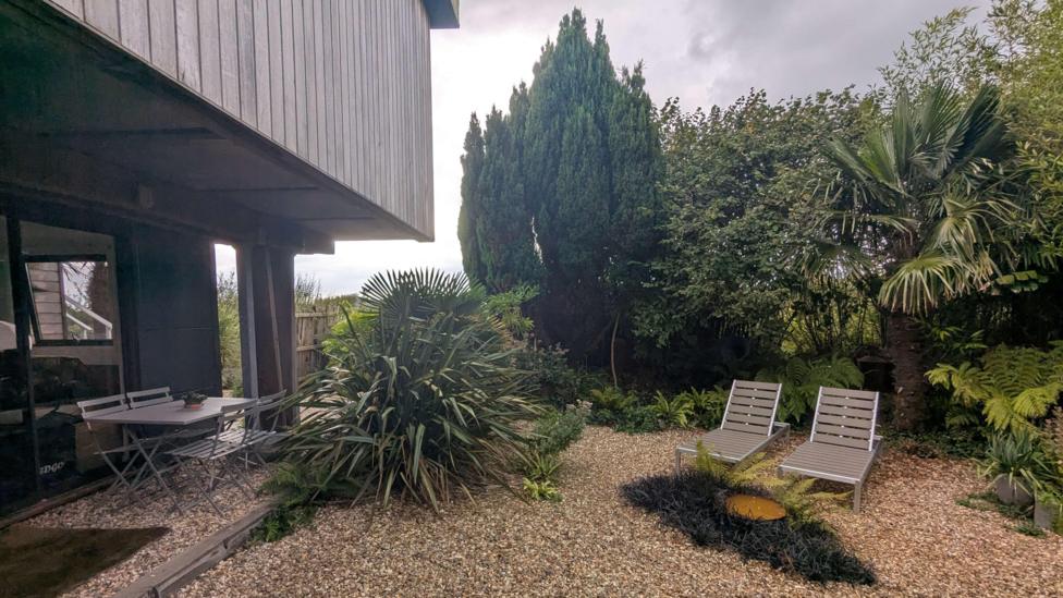 Two garden chairs outside the home on pebbles surrounded by greenery.