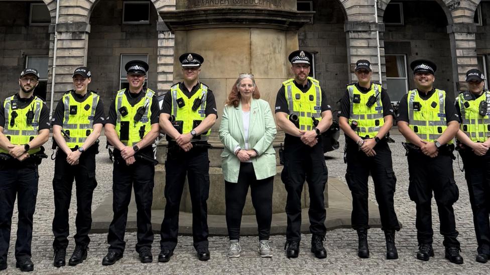 Uniformed police officers standing in a row in front of the City Chambers. Councillor Margaret Graham, who is wearing a mint green blazer and black trousers stands in the middle.
