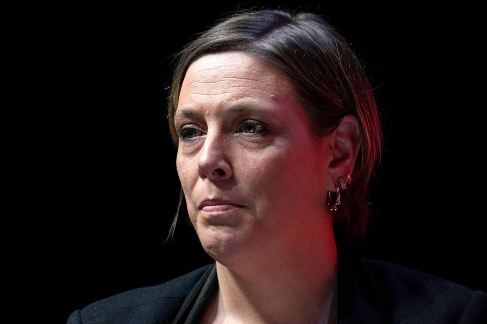 Close-up portrait of Jess Phillips on a dark stage or event set, wearing a dark jacket and multiple earrings.