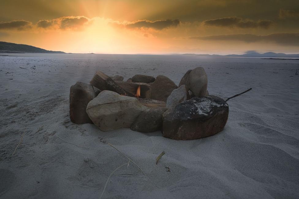Stones with a small fire in the middle on a sandy beach at sunset