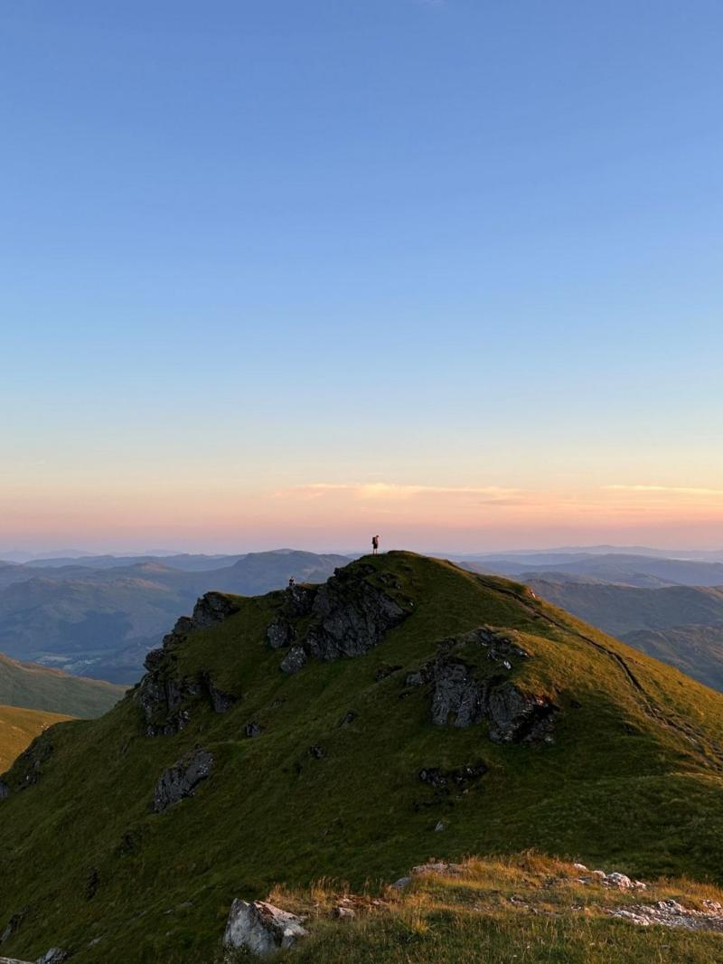 A mountain with hills in the background. A person is on top of the mountain