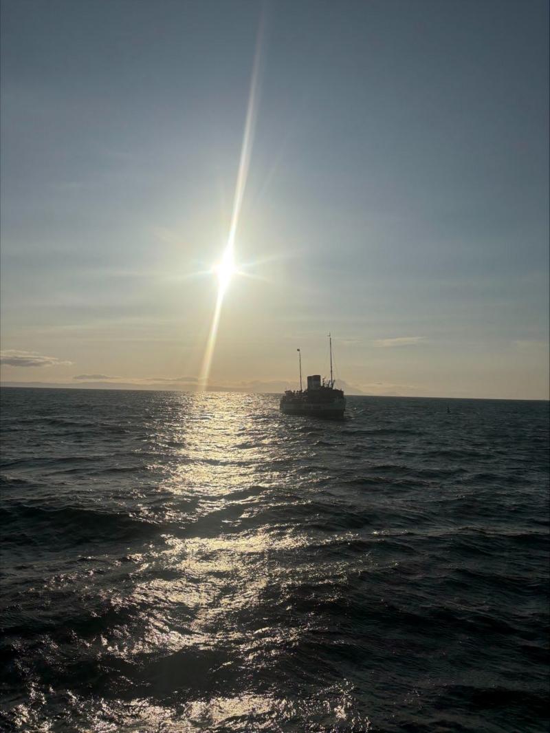 A boat silhouetted with the sun in the background. The water is choppy.