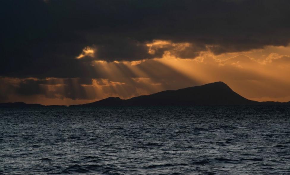 Light shines through dark clouds over a hill and loch
