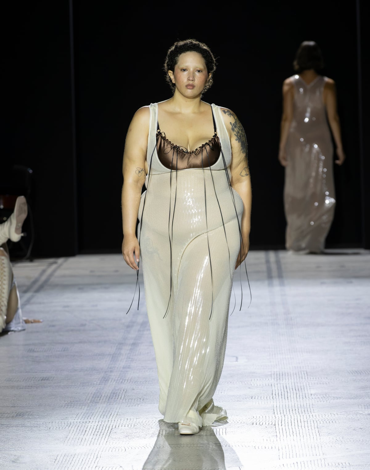 Model wearing white sheer dress with black bodice on catwalk