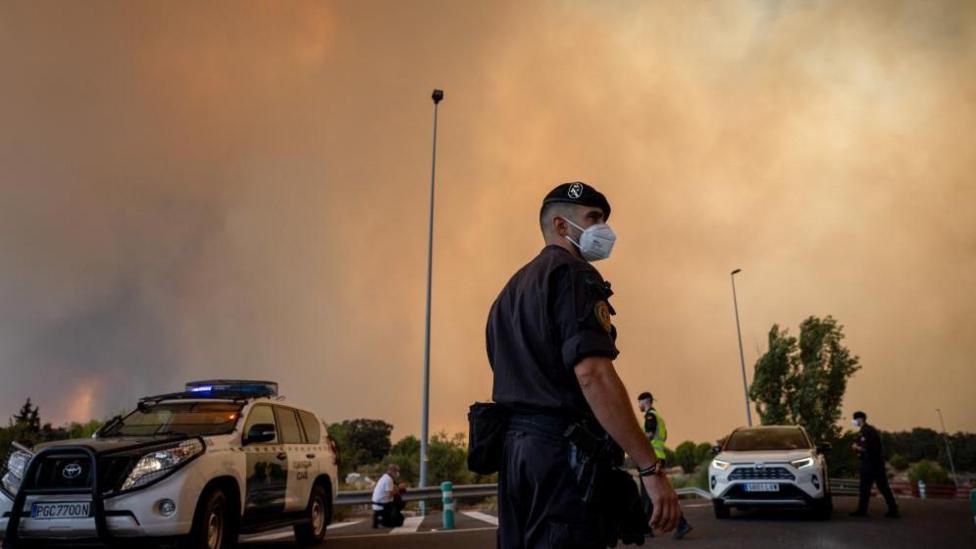 A Civil Guard officer wears a protective mask as smoke from a wildfire obscures the sky in Cenicientos, Madrid, Spain.