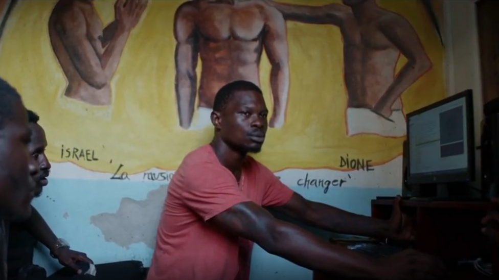 Rapper Stone uses a computer. Two men watch him.