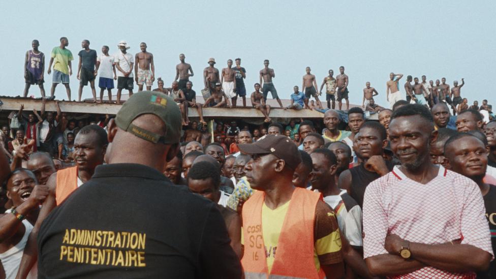 Inmates form a crowd in the courtyard - some of them can be seen standing on a corrugated iron roof.