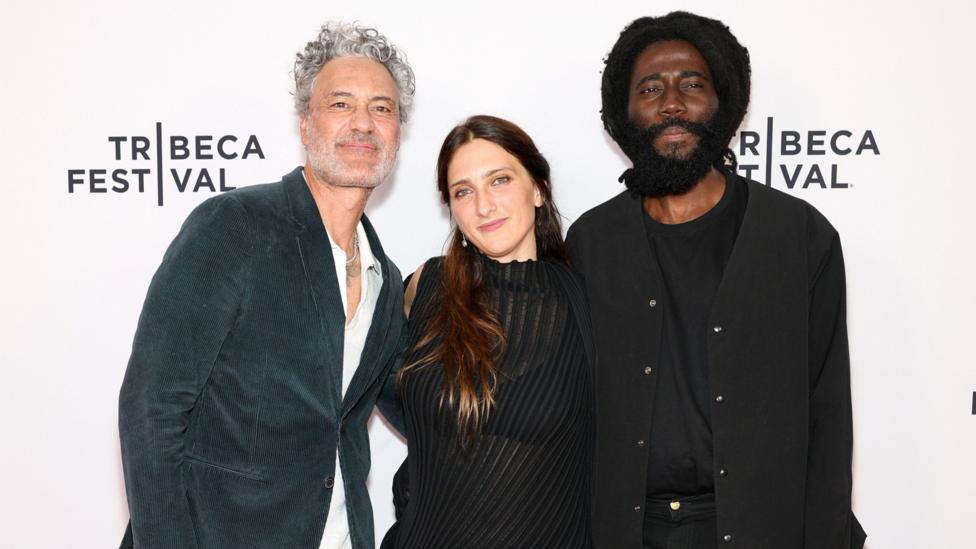 Taika Waititi, Dione Roach and Steve Happi pose for a photo in front of a Tribeca Festival step and repeat