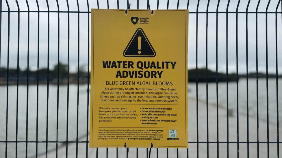 A yellow warning sign has been attached to a black fence. it reads: 