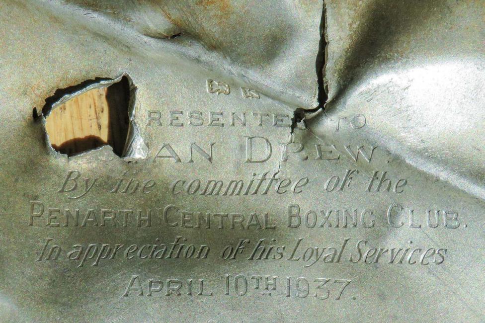 In the top left, jagged edges indicate that a high-velocity round has passed through the silver, rendering some of the writing indistinguishable