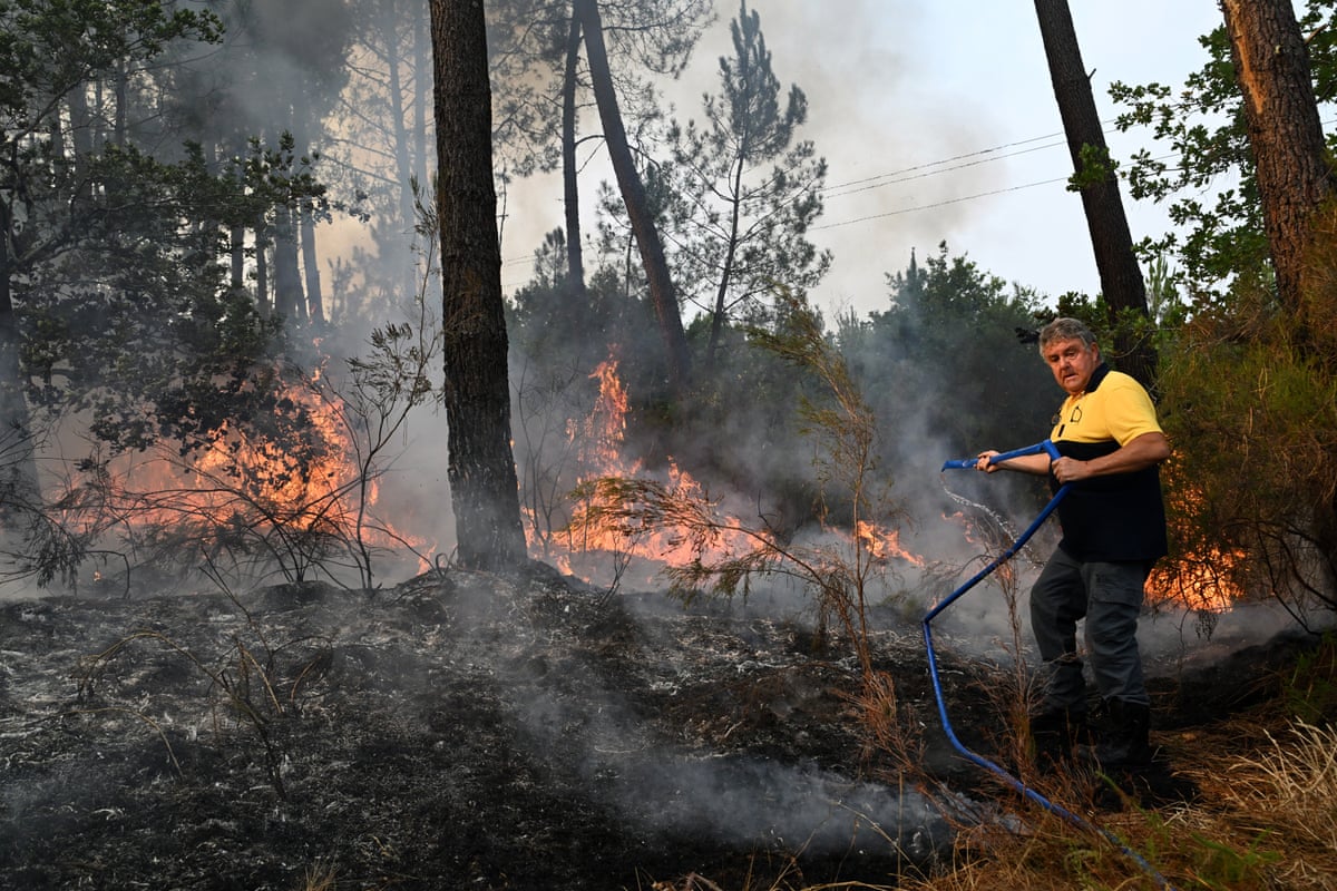 A local resident uses a hose to put out flames burning across the road from his house near Marcheprime, outside Bordeaux in France.