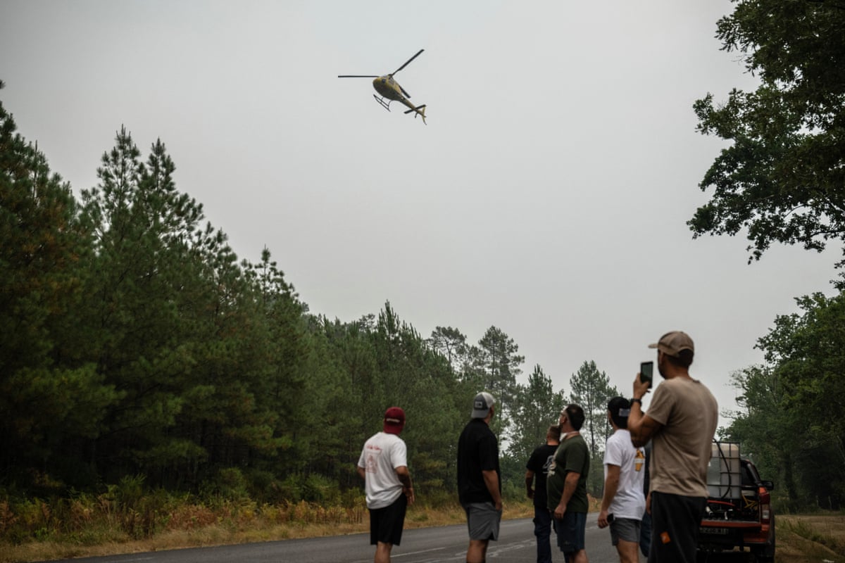 Residents look at a helicopter flying overhead while a wildfire burns