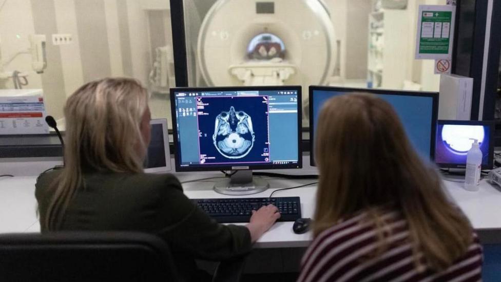 Two people look at a computer screen with image of brain