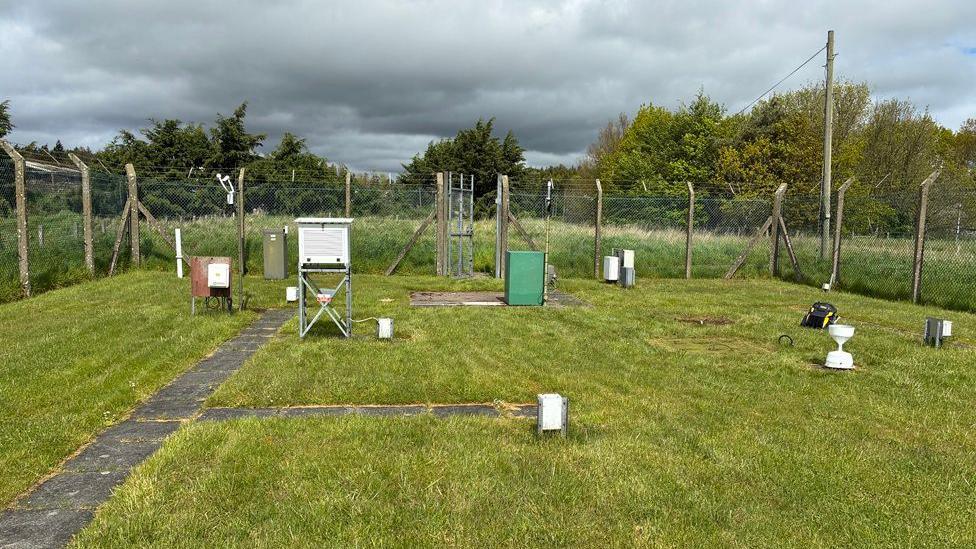 A fenced off area containing weather recording equipment surr
