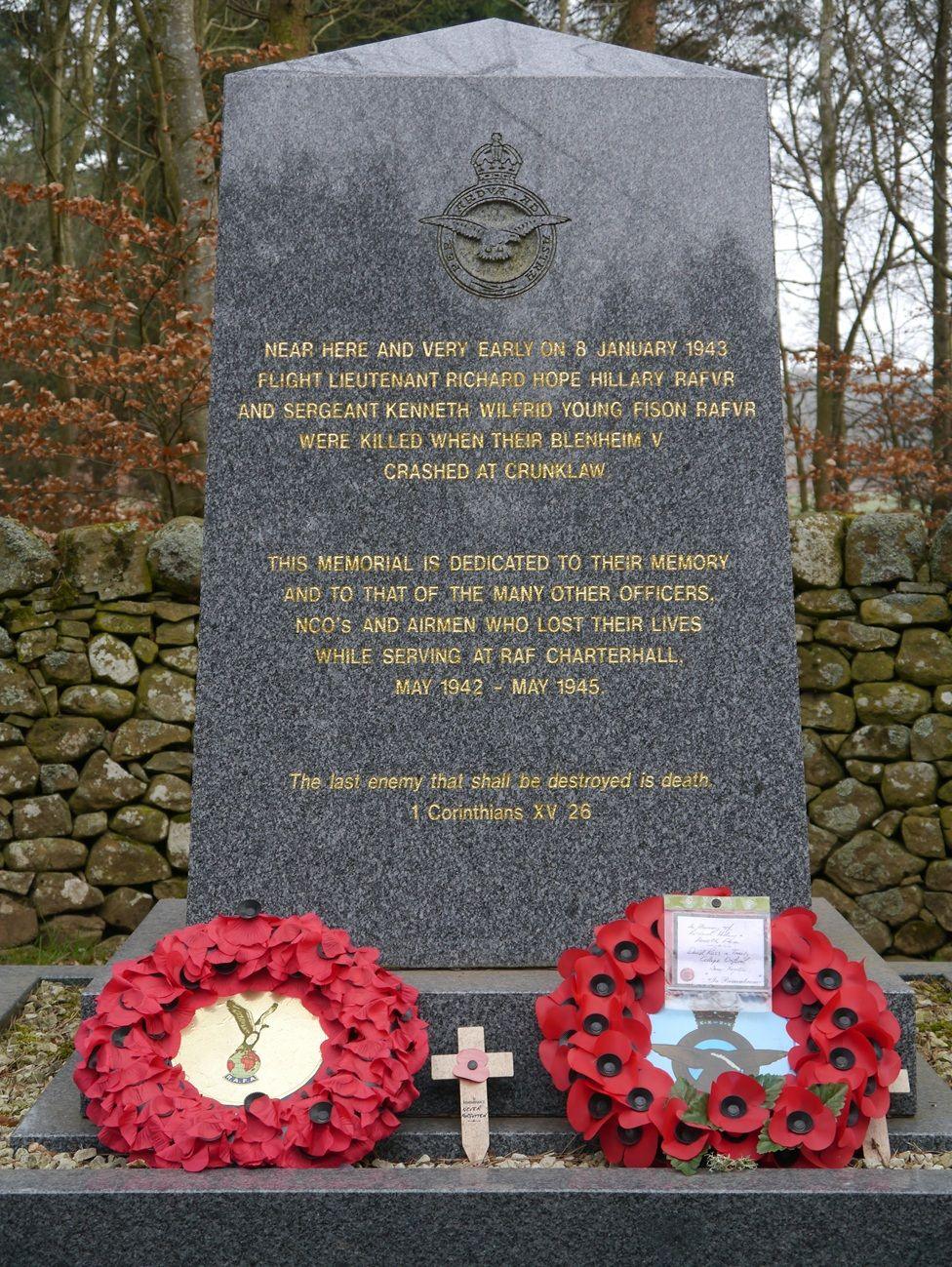 A large memorial with gold typeface on black marble and two poppy wreaths lying on top of it