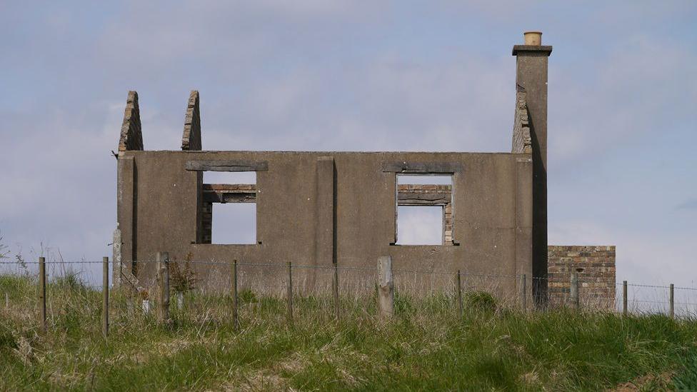 A derelict building with no roof, windows missing and a chimney