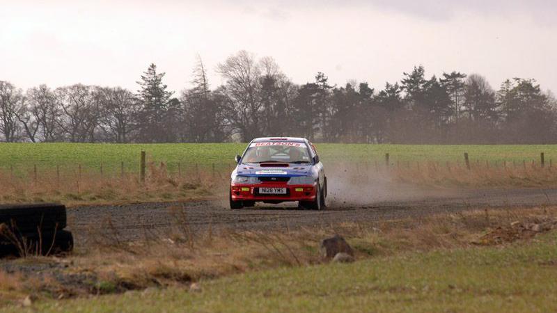A rally car throwing up dust as it travels across a road in the rural Borders