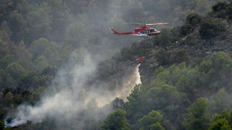 A firefighting helicopter dumps water on a wildfire near Betxi, north of Valencia in Spain.
