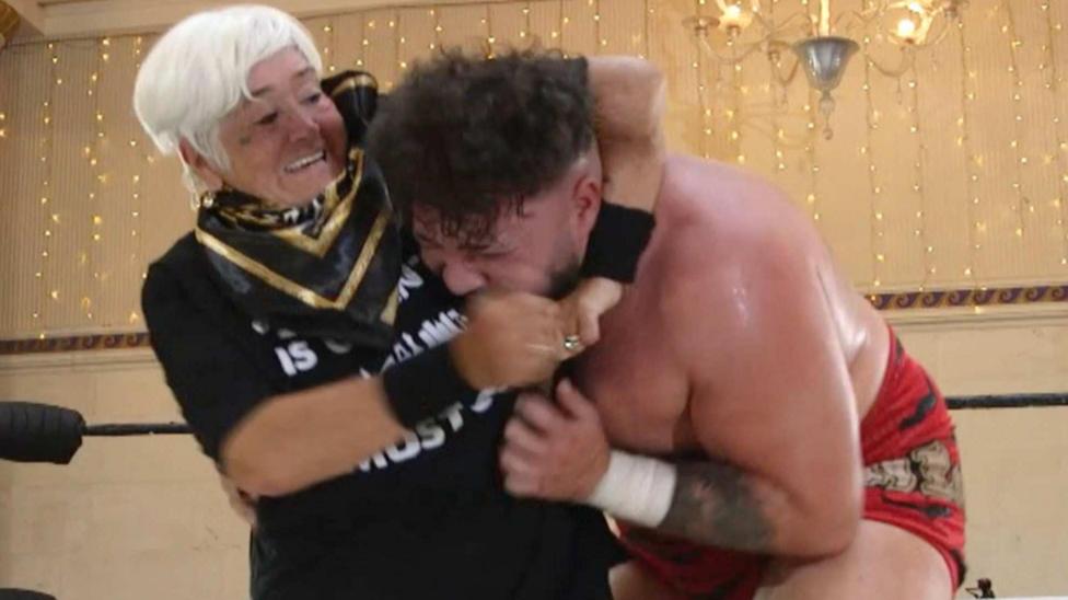 Susie Matthews, 73, taking part in wrestling showcase in Cardiff. She has a male professional wrestler in a headlock.