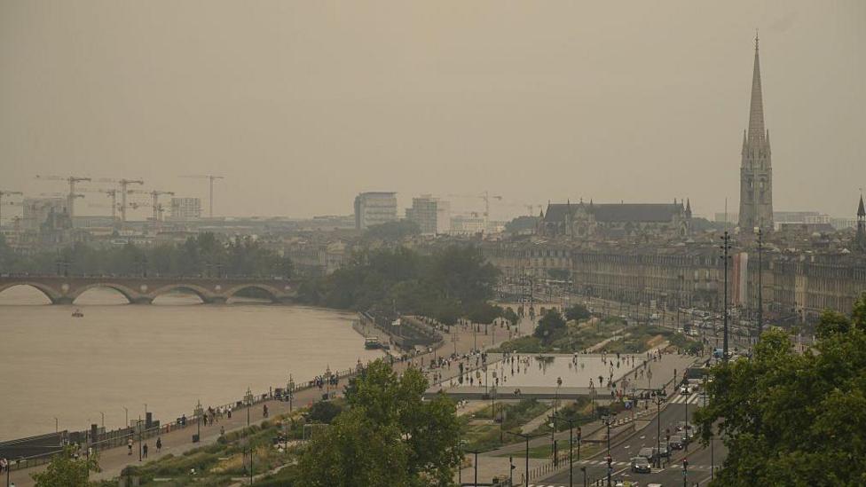 Brown-tinged image of the city of Bordeaux, over which visible thick smoke has darkened the sky