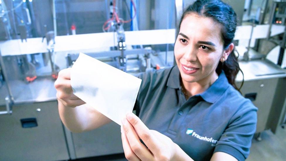 A female Fraunhofer worker holds up some paper which has been sealed using a laser sealing process.