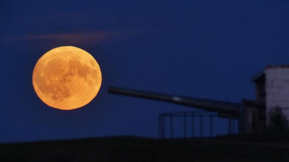 An image of a Buck Moon (which looks like a golden yellow) to the left of a canon coming from the right. 