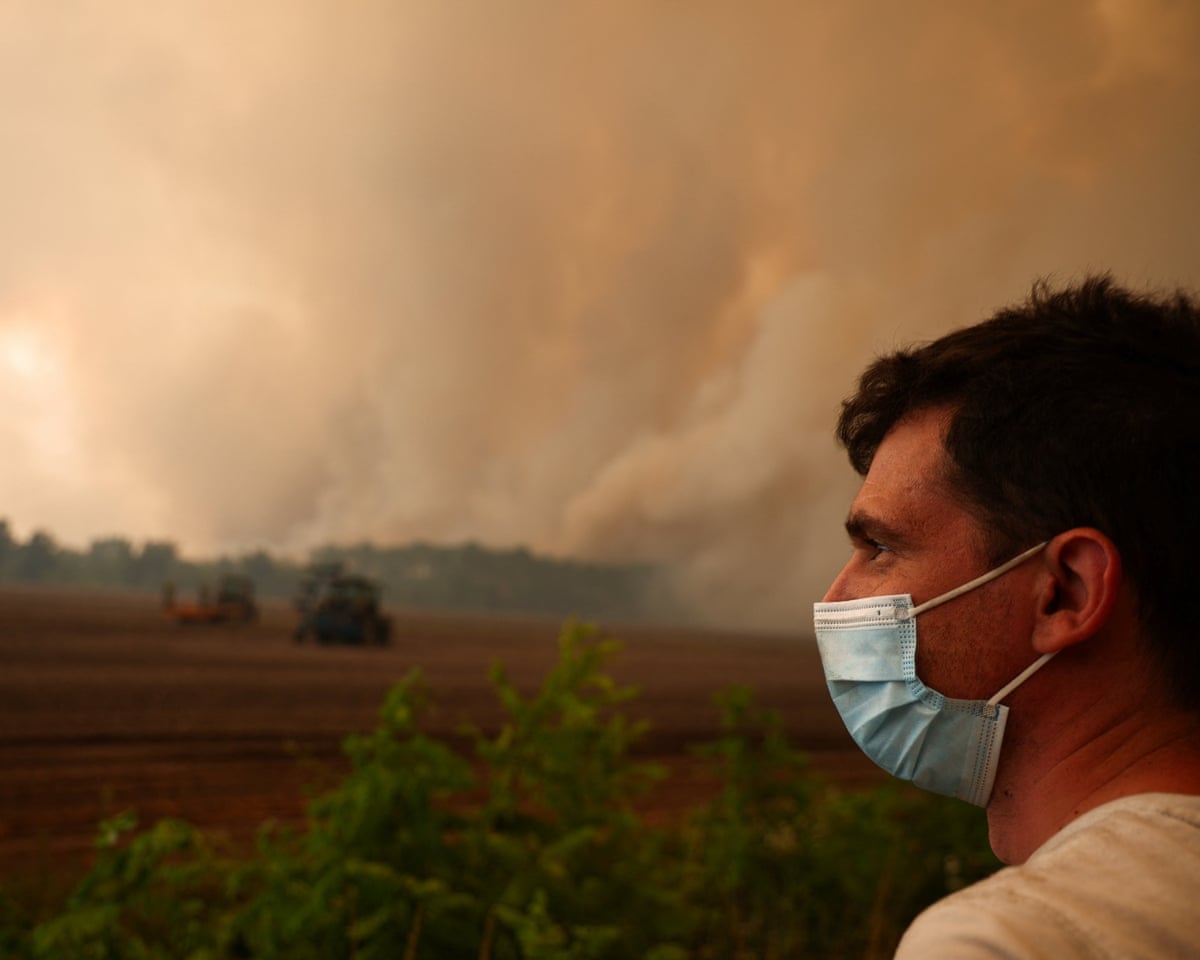 A man wears a mask, while smoke rises from a wildfire in Pierroton, Gironde, France.