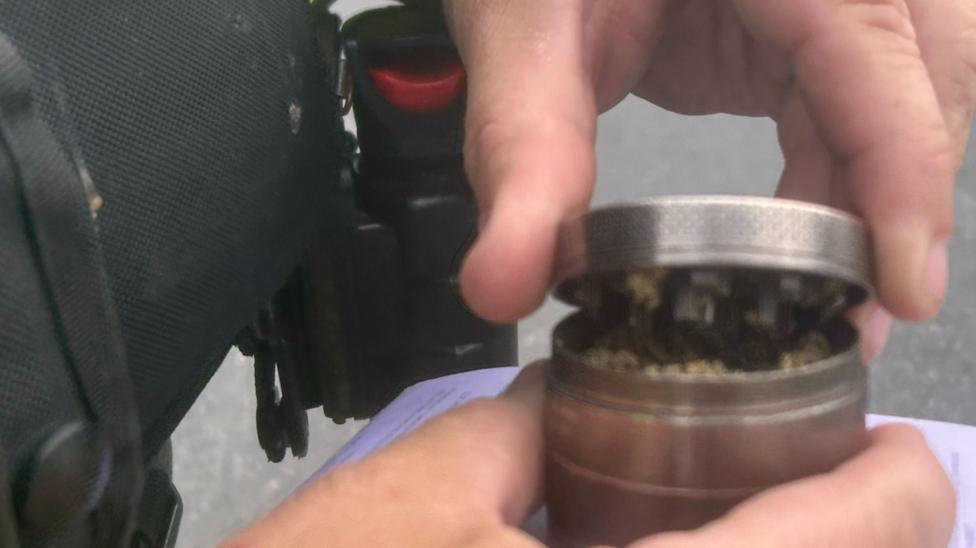 A close up of an officer's hand holding a small metal container. 