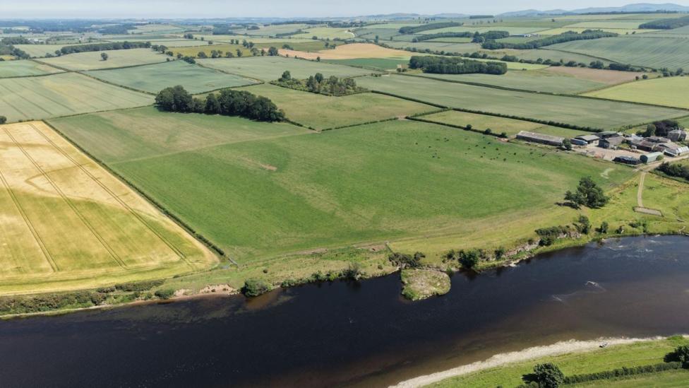 An aerial shot looking down across green and yellow fields with a river in the foreground