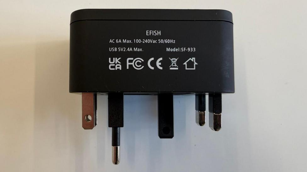 A universal travel adaptor, with information and safety markings displayed on its black plastic casing, is shown with all its pins retracted at once.